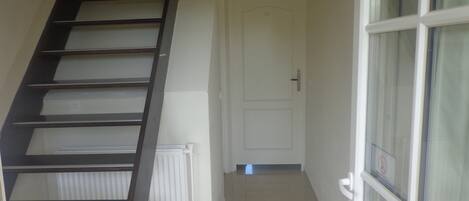 Un escalier menant à un palier où se trouve une porte blanche et une fenêtre avec un vitrage dépoli.