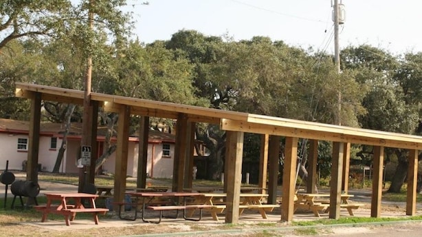 Ein hölzernes Pavillon mit Picknicktischen, ein Gebäude im Hintergrund und Bäume.