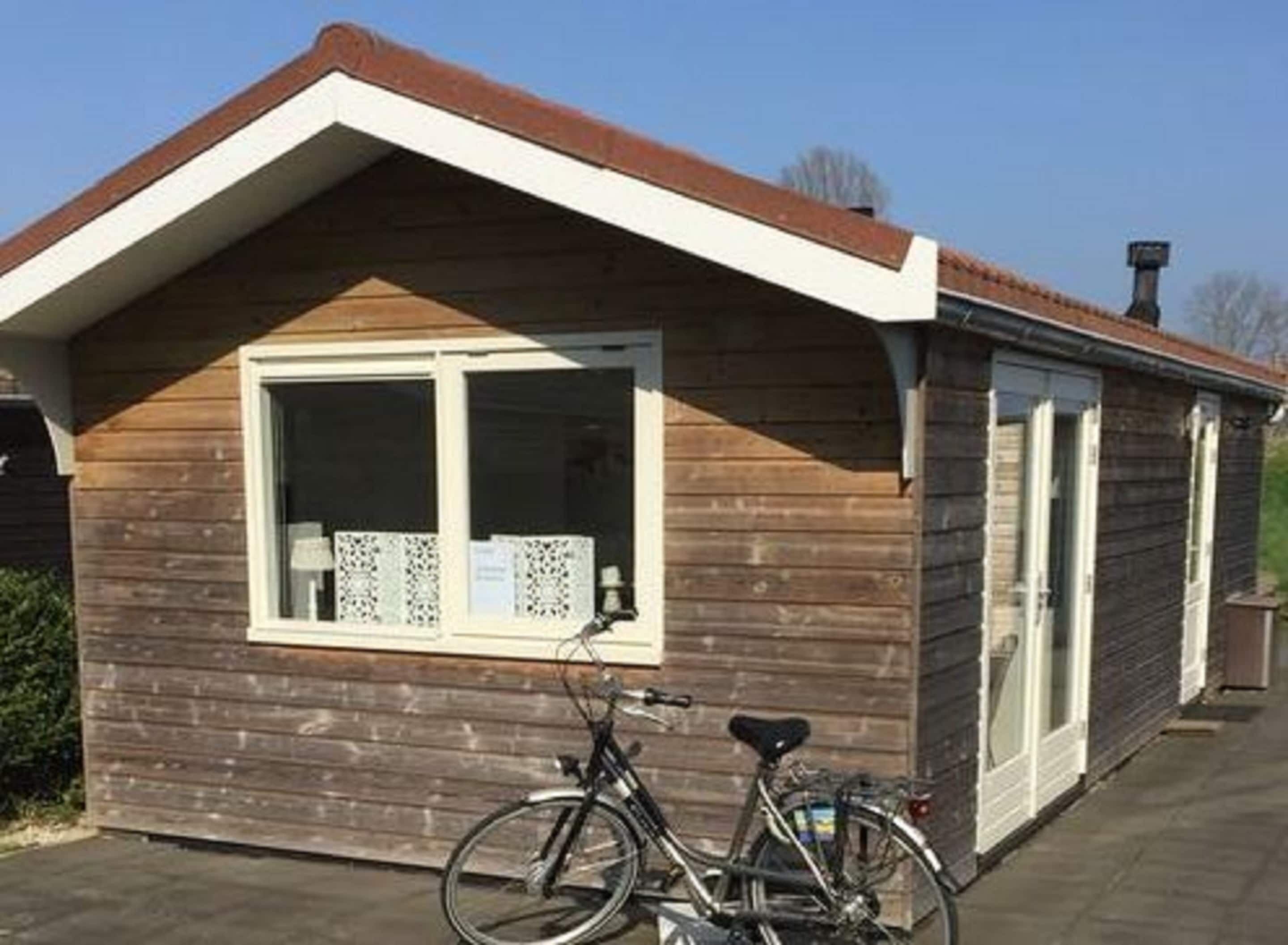 A small wooden building with a pitched roof, a window with a white frame, and a bicycle parked in front.