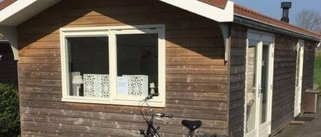 A small wooden building with a pitched roof, a window with a white frame, and a bicycle parked in front.