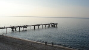 A pier extending into calm waters with a pebbled beach in the foreground.