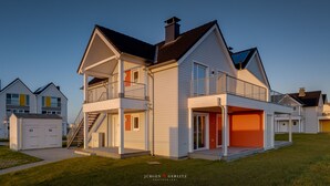 A two-story residential building with a balcony, a garage, and a staircase leading to the upper floor. - Ostseeskipper - Whirlpool, Shower, Fireplace, Infrared Sauna, 1st Floor, Grill (Olpenitz)