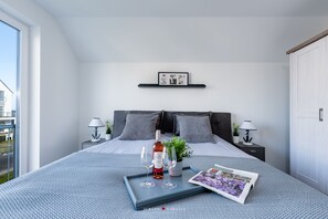 A modern bedroom with a large bed, two bedside tables with lamps, a small potted plant, a tray with wine glasses, and a magazine.