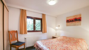 Une chambre à coucher comprenant un lit, une chaise, une fenêtre avec des rideaux, un radiateur, une lampe fixée au mur et un tableau.