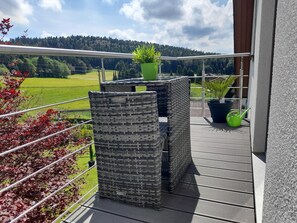 A balcony with wicker furniture, a potted plant, and a view of a green field and forest. - Attic Apartment, Herrischried (Herrischried)