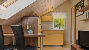Une cuisine compacte avec une fenêtre, un coin repas avec des chaises et un téléviseur posé sur un meuble en bois.