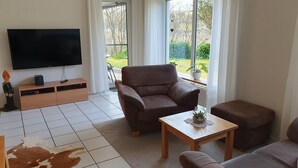Una sala de estar con un sofá de cuero marrón, una mesa de centro de madera, un televisor de pantalla plana y un mueble de madera.