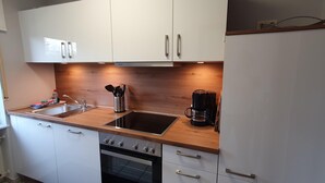 Una cocina compacta con armarios blancos, un lavamanos de acero inoxidable, una cafetera y un horno empotrado.