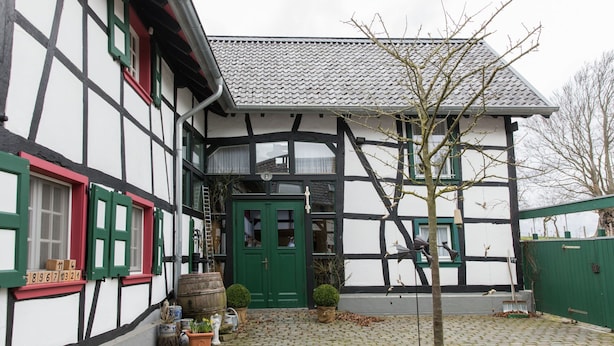 Ein traditionelles Fachwerkhäuschen mit grüner Tür, Blumentöpfen und einem Kopfsteinpflasterhof.