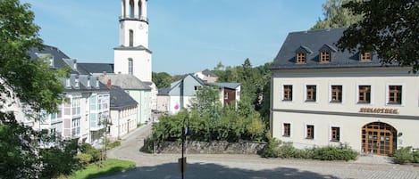 A town square with cobblestone pavement, a church tower, and buildings with traditional architecture.