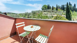 A balcony with a table and chairs, overlooking a garden with trees and shrubs. - Villa in Monterotondo With Pool & Tiber Views (Monterotondo)