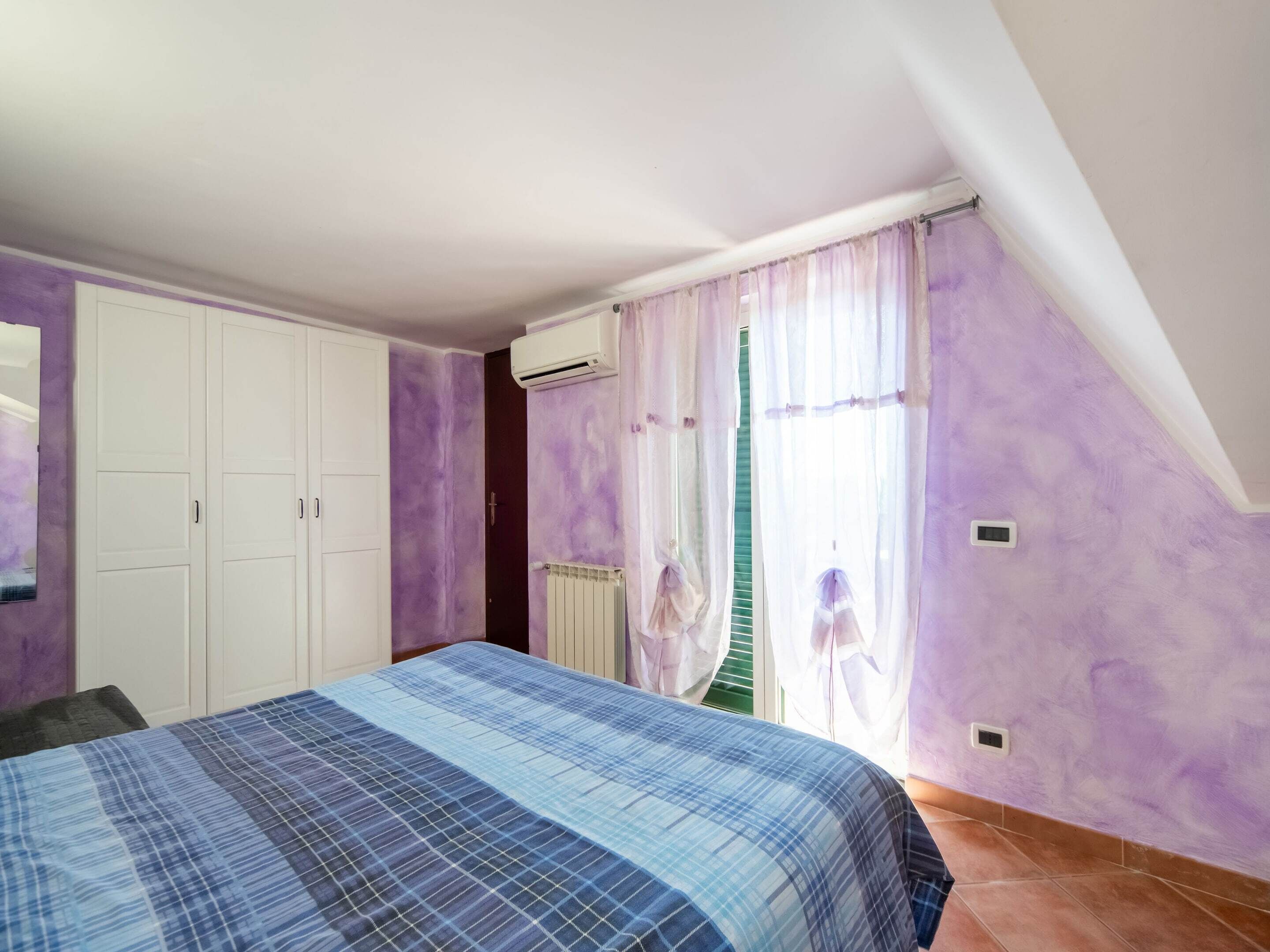 Une chambre à coucher avec un lit, une armoire, un radiateur et une fenêtre avec des rideaux.