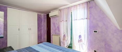Une chambre à coucher avec un lit, une armoire, un radiateur et une fenêtre avec des rideaux.