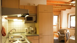 A compact kitchen with a microwave, coffee maker, and stove. There is a wooden dining area with a chair and table. - Apartment Near Willingen & Winterberg Ski Slopes (Medebach)