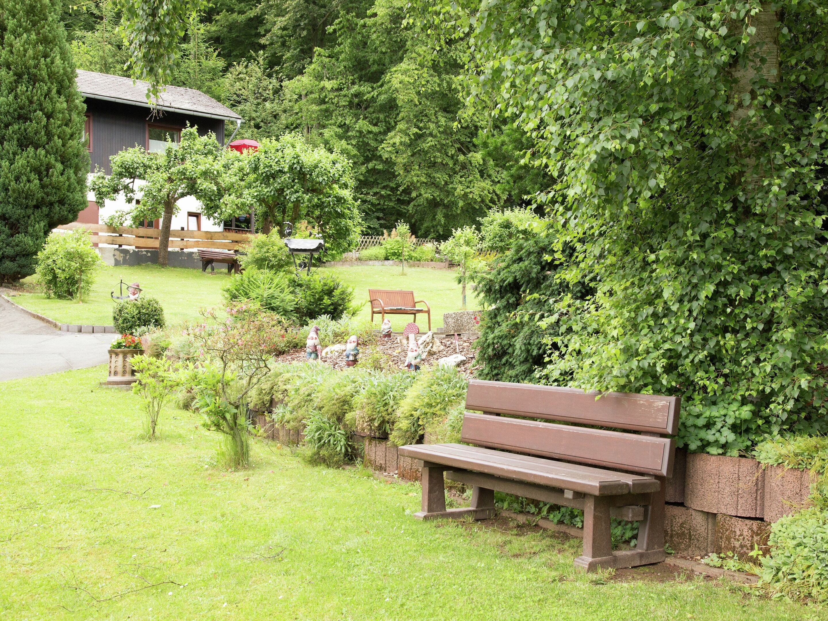 Un parc avec un banc en bois, un jardin avec différentes espèces de plantes et un bâtiment en arrière-plan.