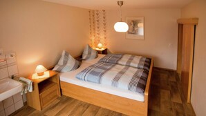 A bedroom with a wooden bed, two bedside tables with lamps, a wooden wardrobe, and a bathroom with a sink and towel rack. - Apartment Near Willingen & Winterberg Ski Slopes (Medebach)