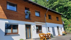 A two-story building with a wooden facade and white walls. There is a balcony with a metal railing and potted plants. - Apartment Near Willingen & Winterberg Ski Slopes (Medebach)
