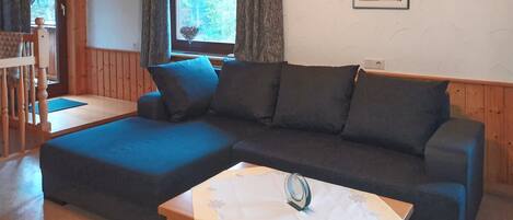A modern living room with a sectional sofa, a wooden coffee table, and a window with curtains.
