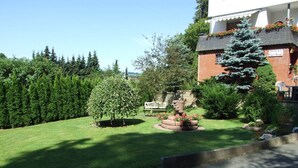 A well-maintained garden with a lawn, a small tree, and a stone planter with flowers. - Apartment Near Willingen & Winterberg Ski Slopes (Medebach)