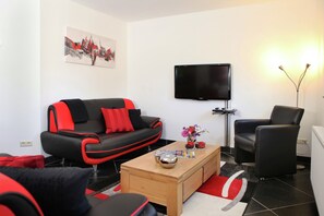 A modern living room with a black and red sofa, a flat-screen TV, a wooden coffee table, and a black armchair. - Holiday Home in Epen With Garden & BBQ (Epen)