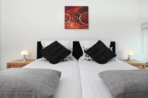 A double bed with black and white patterned pillows, a red abstract painting on the wall, and two bedside lamps on wooden nightstands.