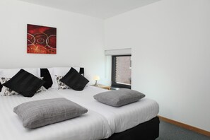 A hotel room with a large bed, a window with a view of a brick building, and a red abstract painting on the wall. - Holiday Home in Epen With Garden & BBQ (Epen)