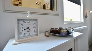 A framed London clock on a white mantelpiece, a window with a view, and a tray with jars and a rope handle.