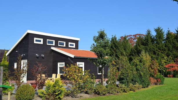 A two-story house with a red roof, surrounded by a well-maintained garden and trees.