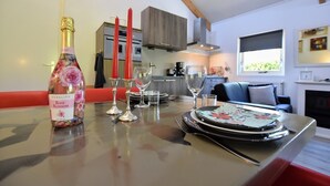 A dining table set with a bottle of sparkling rose blossom wine, red candles, and clear glasses.