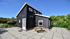A black building with a white door and windows, a paved patio with a picnic table, and a clear blue sky.