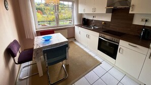 A compact kitchen with white cabinets, a built-in oven, and a window with a view of greenery. - Einladende Ferienwohnung in Muellenborn Eifel (Gerolstein)