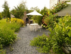 Relax in a serene garden setting with a patio featuring a round table and four chairs, shaded by a white umbrella.