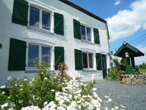 A two-story building with green shutters, a stone wall, and a statue in the garden.