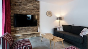Een moderne woonkamer met een stenen muur, een flatscreen-tv, een bank, gestreepte fauteuils, een salontafel en een klok.