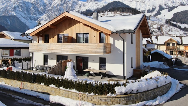 Een modern chalet met twee verdiepingen, houten gevel, grote ramen en een balkon.