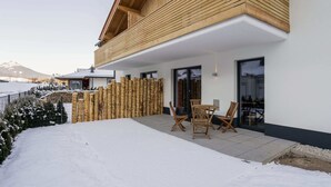 Een modern gebouw met een houten balkon, een overdekt terras en een besneeerd landschap op de achtergrond.