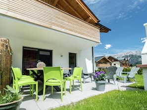 A modern outdoor seating area with green chairs and a table, surrounded by a well-maintained lawn and a mountain backdrop.