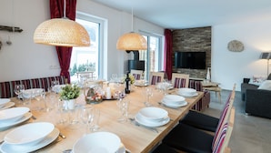 Een moderne eetruimte met een lange houten tafel, gedekt voor een maaltijd, grote geweven lampen en een accentmuur van steen.
