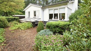 A modern house with a large glass window, surrounded by a well-maintained garden with various plants and flowers. - Holiday Home in Holten Near Holterberg (Holten)