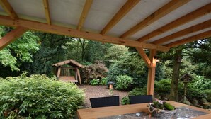 An outdoor wooden pergola with a table and chairs, surrounded by lush greenery and a garden. - Holiday Home in Holten Near Holterberg (Holten)