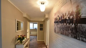 A hallway with a wooden floor, a white console table with a vase of flowers, a mirror, and a wall-mounted picture. - Holiday Home in Holten Near Holterberg (Holten)