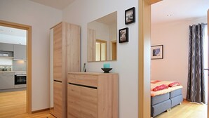 A modern apartment with a wooden wardrobe, a kitchen in the background, a grey sofa, and a patterned curtain. - Apartment in Heinrichskirchen (Roetz)