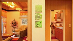 A room with a checkered floor, a chair, a table with a vase, and a window with curtains. - Waldblick Forest Retreat (Schmogrow)