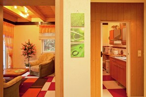 Una habitación con suelo a cuadros, una silla, una mesa con un florero y una ventana con cortinas.