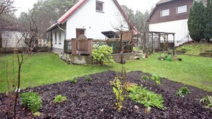 A house with a white exterior and red roof, surrounded by a garden with raised beds and a wooden fence. - Waldblick Forest Retreat (Schmogrow)