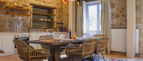 A rustic kitchen with stone walls, wooden shelves, and a dining table with wicker chairs.