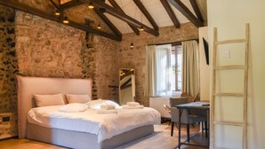 A bedroom with a stone wall, wooden beams, a bed with white linens, a desk, and a chair. - Secluded Mountain Refuge - Theonimfi Paradise Gem (Gortynia)