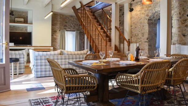 A dining area with a wooden table, wicker chairs, and a staircase leading to an upper floor. - Secluded Mountain Refuge - Theonimfi Paradise Gem (Gortynia)