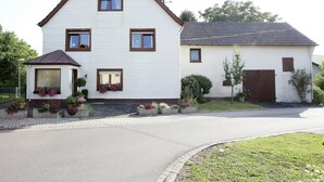A two-story house with a triangular roof, a small attached garage, and a front garden with potted plants. - Spacious Apartment in Pracht near Forest (Pracht)