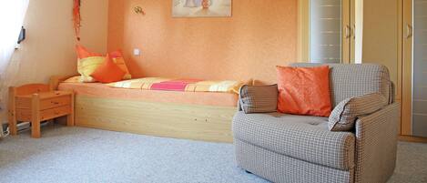 Un dormitorio con cama, una silla, una mesita y un armario.